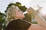 Mid adult woman in sunlit park drinking lemonade