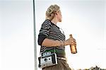 Mid adult woman carrying beer bottle and vintage camera in park