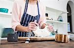 Cropped shot of young woman stretching dough at kitchen counter