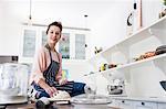 Portrait of young woman sitting on kitchen counter preparing dough