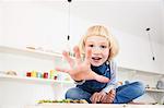 Portrait of cute girl sitting on kitchen counter reaching out her hand