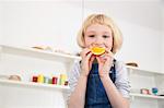 Portrait of cute girl in kitchen holding orange slice to her mouth