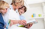 Mature woman sitting on kitchen counter reading storybooks with son and daughter