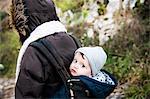 Portrait of baby boy wearing knit hat, carried in baby sling by mother