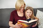 Grandmother and granddaughter reading book on sofa