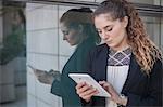 Young businesswoman, standing outdoors, beside window, using digital tablet