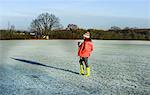 Woman walking across snowy field, carrying young baby in sling, rear view