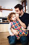 Mature man whispering to his daughter in kitchen