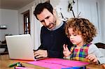Girl drawing at table while father using laptop