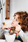 Girl looking up while having cereal in kitchen