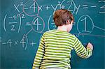 Rear view of primary schoolboy answering equation on classroom blackboard