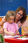 Preschool girl and teacher with colouring pens in classroom