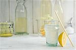 An elderflower drink in a glass with a straw and homemade elderflower cordial in bottles