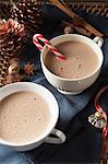 Two large white mugs of frothy hot chocolate (one with a candy cane) for Christmas