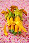 A bunch of yellow courgettes with flowers tied together with a ribbon on a floral tablecloth