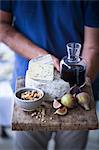 A man holding a cheese board with blue cheese, figs, nuts and wine