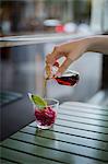 A hand pouring herb liqueur on pomegranate granita in a glass