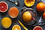 Manual metal citrus fruit extractor next to glasses of orange juice and red grapefruit juice and whole and half cut oranges and red grapefruit