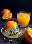 Manual glass juicet extractor with squeezed oranges and a glass of orange juice on a dark slate