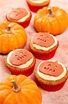 Several Pumpkin pie cupcakes shown with real pumpkins on a light orange background