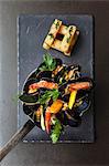 A pan of mussels with prawns, corn and vegetables served with a stack of chunky chips