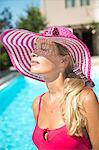 Close-up of young woman with a sunhat on the edge of a swimming pool.