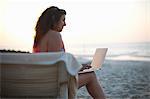 Mature woman sitting on beach sun lounger looking at laptop, Dubai, United Arab Emirates