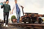 Two young men walking along train track, carrying skateboards, Bristol, UK