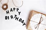 Gift wrapped in brown paper, doily and string, beside letters spelling Happy Birthday