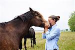 Woman with her face to horse's muzzle in field