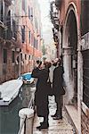 Couple photographing building exteriors from canal waterfront, Venice, Italy