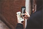 Over the shoulder view of man holding two smartphones with photographs of alley, Venice, Italy