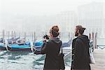 Couple photographing gondolas on misty canal, Venice, Italy