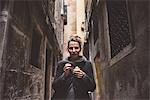 Portrait of young woman eating gelato in dark alley, Venice, Italy