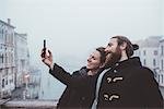 Couple taking smartphone selfie over misty canal, Venice, Italy