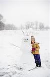 Girl shovelling snow in front of snowman, Lakefield, Ontario, Canada