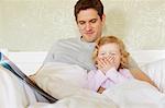 Female toddler yawning in bed with father
