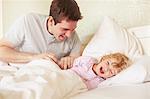 Mid adult man tickling toddler daughter in bed
