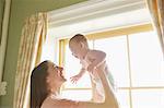 Mid adult woman holding up baby daughter in bedroom