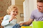 Mid adult man and toddler daughter eating bread at kitchen table