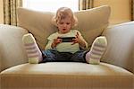 Female toddler sitting on armchair playing hand held computer game