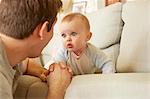 Cute blue eyed baby girl on sofa staring at her father