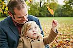 Daughter sitting on father's lap holding autumn leaf