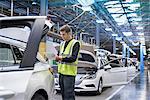 Apprentice car inspector using tablet in car factory