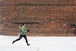 Young female runner in knit hat running along snow covered sidewalk