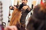 Male hairdresser blow drying customer's red hair in hair salon