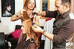 Hairdressers using curling tongs on customers long red hair in salon