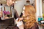 Hairdresser showing customer styled long red hair in salon