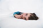 Boy lying between white bed sheets