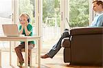 Boy at desk and father on sofa using laptops